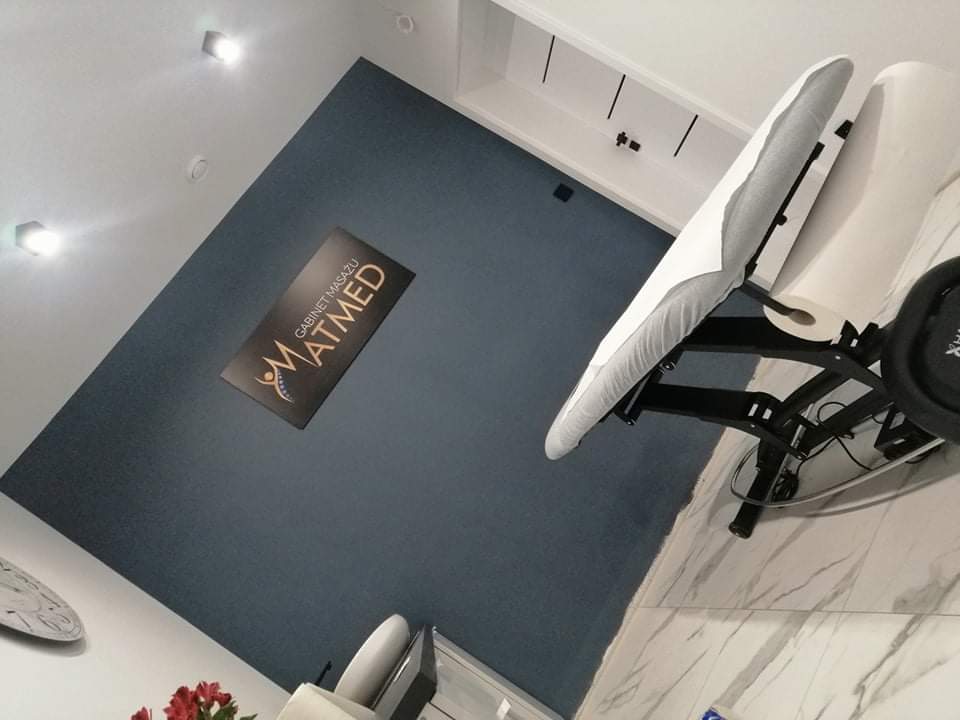 Gabinet MATMED, grafitowa tablica ze złotym logo widziana z perspektywy leżanki na białym marmurze.